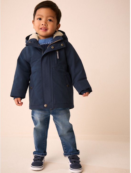 Jongetje in donkerblauwe parka, blauwe trui en spijkerbroek. De jas is open.