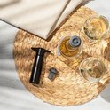 Zwarte Vacu Vin wijnstopper met een fles witte wijn en twee glazen op een rieten onderzetter.