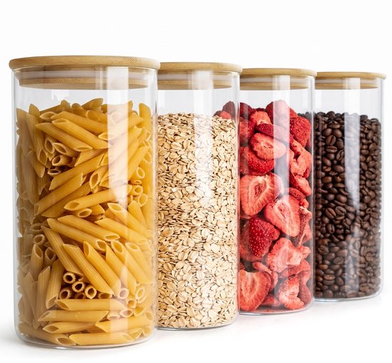 Vier glazen voorraadpotten met bamboedeksel, gevuld met penne pasta, havermout, gedroogde aardbeien en koffiebonen.