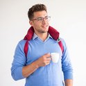 Man met bril met een rode warmtekussennekband, houdt een witte mok vast.