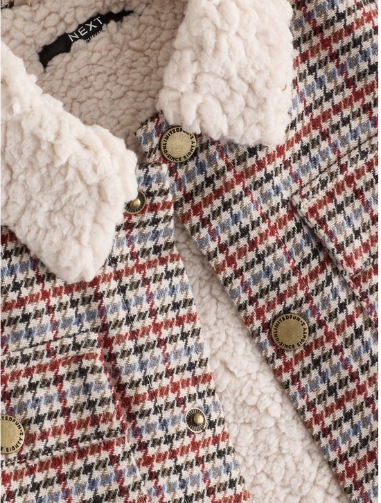 Detail van de borgkraag met label en koperkleurige knopen met tekst 'Unlimited Fun Since Eighty'.