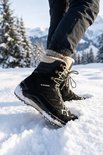 Een persoon draagt zwarte, hoge wandelschoenen met beige bontvoering in de sneeuw.