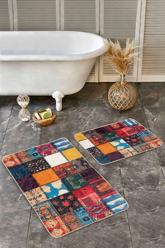 Twee patchwork badmatten met levendige kleuren en patronen, geplaatst op een donkergrijze tegelvloer bij een wit bad.