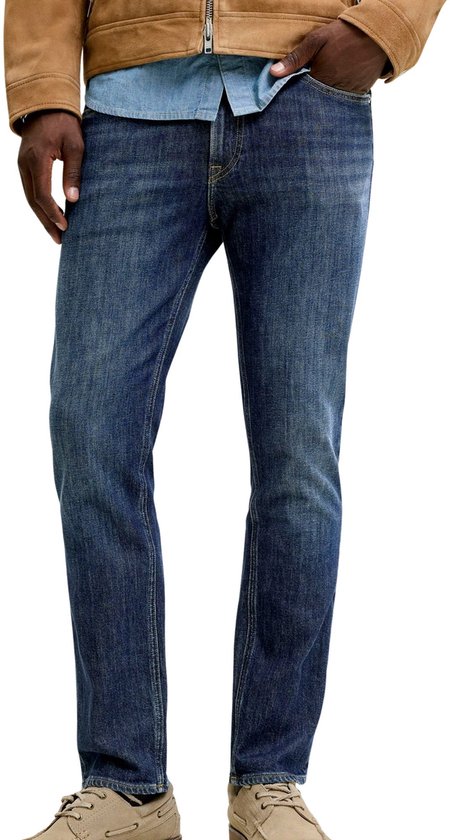Homme portant un jean, une chemise bleu clair et une veste marron.