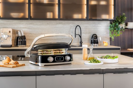 Zwarte contactgrill met gesloten sandwich, in een keukenomgeving.