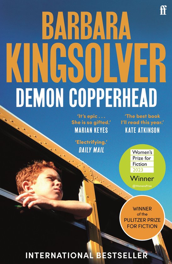 Boek Demon Copperhead van Barbara Kingsolver, met een jongen met rood haar uit een gele schoolbus. "International Bestseller".