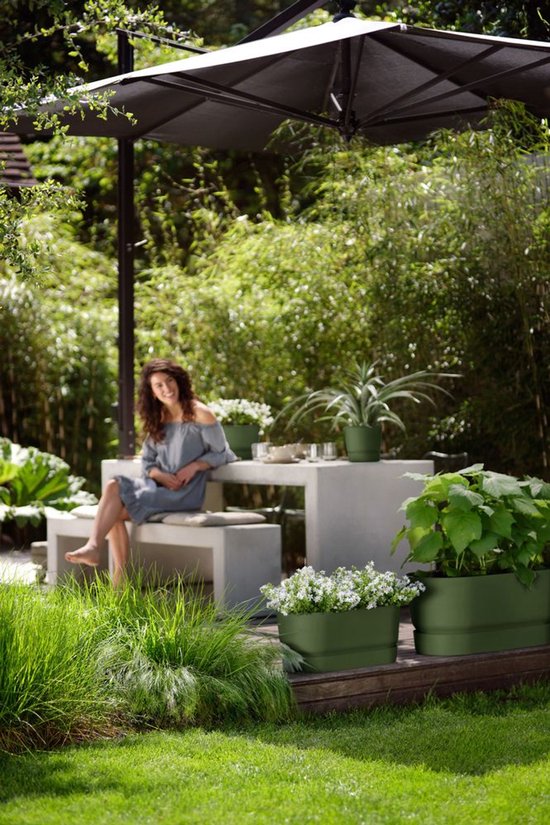 Vrouw op terras met Elho plantenbakken in olijfgroen, gevuld met planten en bloemen.