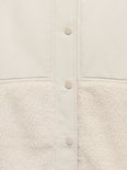 Detail van een lichte teddy jas met knopen en beige sherpafleece.