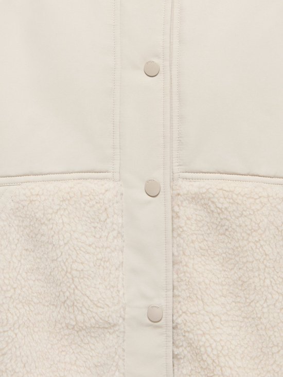 Detail van een lichte teddy jas met knopen en beige sherpafleece.