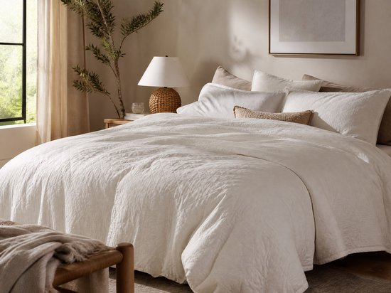 Witte, gewatteerde sprei met ruitpatroon, over een bed met kussens en een plaid.