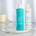 Turquoise fles met "MOROCCANOIL HYDRATING SHAMPOO" en witte fles met "MOROCCANOIL HYDRATING CONDITIONER", beide met oranje M logo.