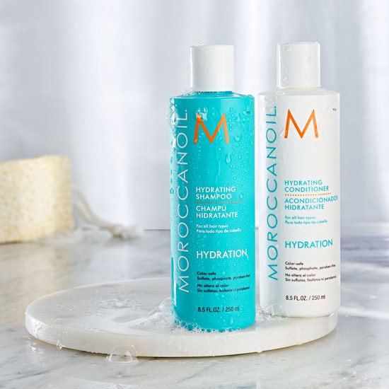 Turquoise fles met "MOROCCANOIL HYDRATING SHAMPOO" en witte fles met "MOROCCANOIL HYDRATING CONDITIONER", beide met oranje M logo.