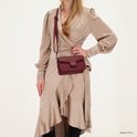 Model draagt bordeauxrode schoudertas, cross-body gedragen over een beige jurk.