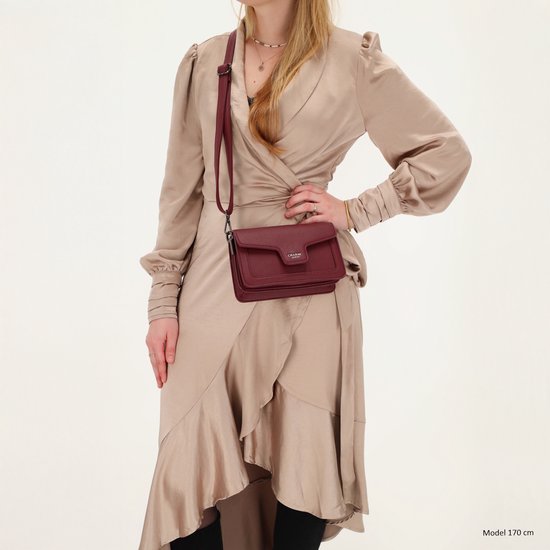 Model draagt bordeauxrode schoudertas, cross-body gedragen over een beige jurk.