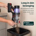 Hand ledigt een transparante stofcontainer van een steelstofzuiger in een zwarte afvalzak.