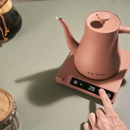 Roze waterkoker op roze basis met digitaal display, hand leest temperatuur af.