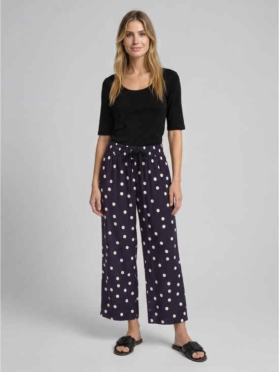 Model in zwarte top en marineblauwe culotte met witte polkadotprint, hoge taille en strikceintuur.