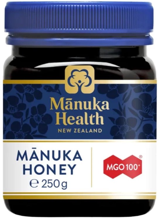Manuka Health honingpot met donkerblauwe deksel. Het etiket is zwart met blauwe bloemen en toont 'Manuka Health NEW ZEALAND', 'MĀNUKA HONEY e 250g' en 'MGO 100'.
