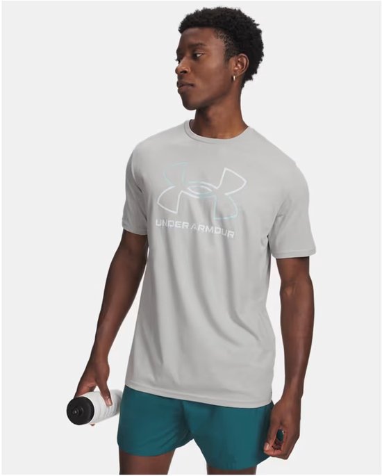 Man draagt een lichtgrijs Under Armour sportshirt met groot logo op de borst. Hij houdt een waterfles vast.