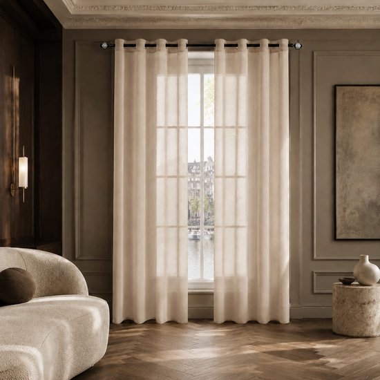 Beige, transparante gordijnen met zilveren ringen hangen voor een raam met uitzicht op een kanaal.
