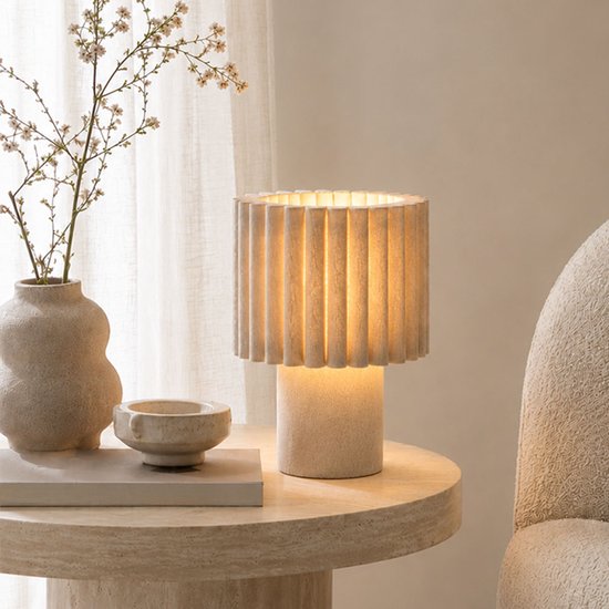 Lampe de table beige avec abat-jour plissé, allumée sur une table d'appoint en marbre.