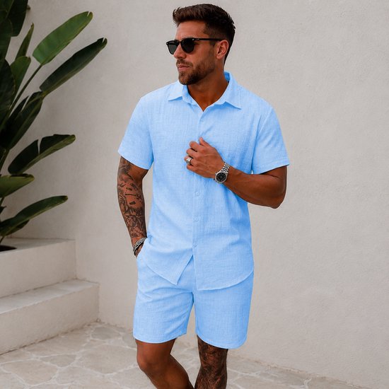 Man, zijaanzicht, draagt lichtblauwe korte mouw blouse en korte broek. Blouse met structuur. Zonnebril.