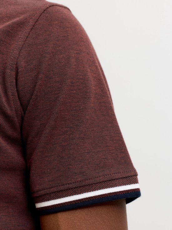 Detail van de mouw van een bordeauxrode polo met witte en marineblauwe streep aan de boord.