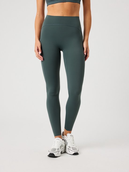 Detail van een donkergroene sportlegging. De legging heeft een hoge tailleband en steekzakken aan de zijkant.