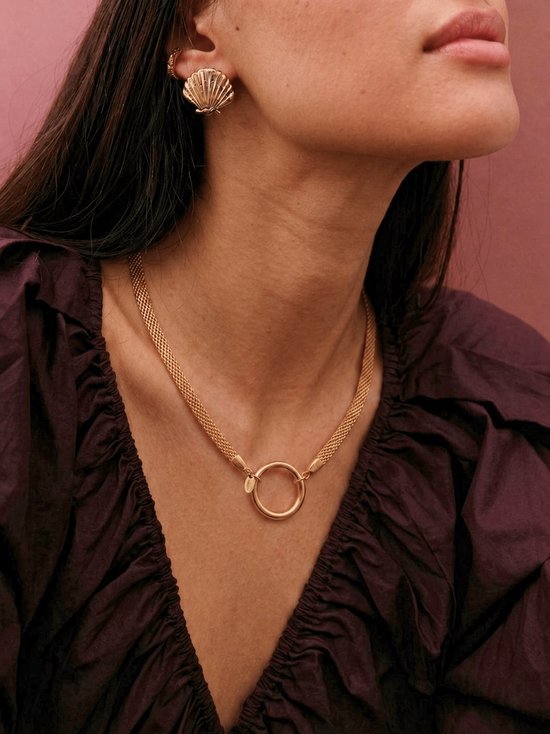 Gouden schakelketting met een gouden ring als sluiting, gedragen door een model.