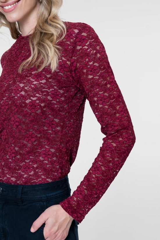 Model in bordeauxrode kanten top met lange mouwen en hoge hals, hand in broekzak.