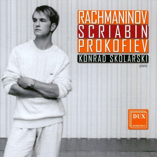 Jonge man in wit kabel gebreide trui en korte broek, poseert met gekruiste armen. Titel: Rachmaninov, Scriabin, Prokofiev, Konrad Skolarski piano.