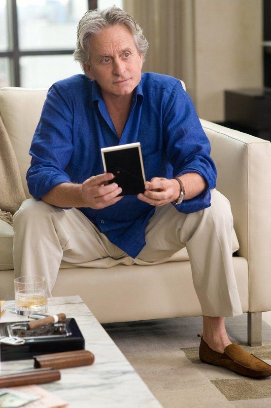 Oudere man in blauw hemd en beige broek zit op bank met fotolijstje.