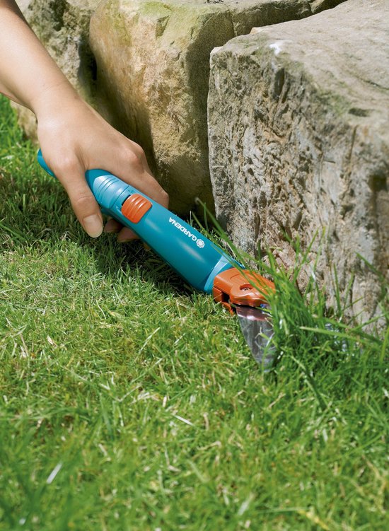 Hand gebruikt blauwe Gardena graschaar om gras te knippen.