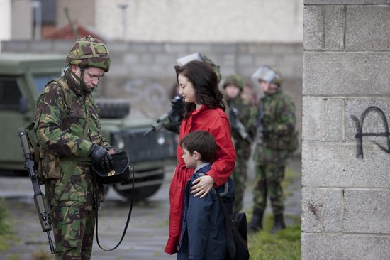 Soldaat in camouflagepak praat met vrouw in rode jas en jongen in blauwe jas.