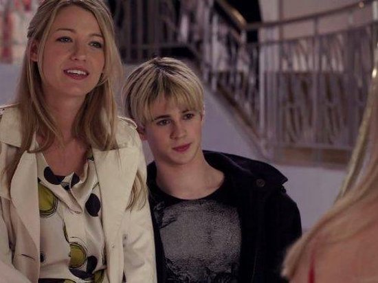 Vrouw met lang blond haar in beige trenchcoat met geprint shirt, naast een jongeman.