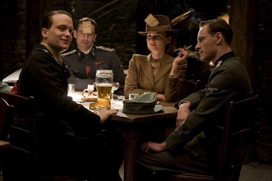 Vier personen aan een tafel met bier en sigarettenrook, waarbij drie mannen militaire uniformen dragen en een vrouw een hoed.