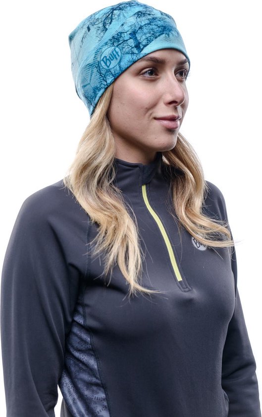 Vrouw met blond haar draagt een blauwe muts met patroon en een grijs vest.