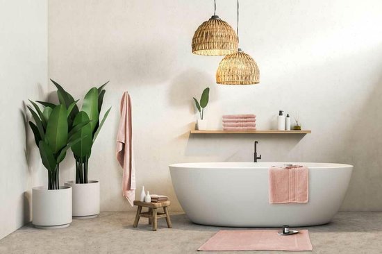 Een lichtroze badmat ligt voor een vrijstaande badkuip in een moderne badkamer.
