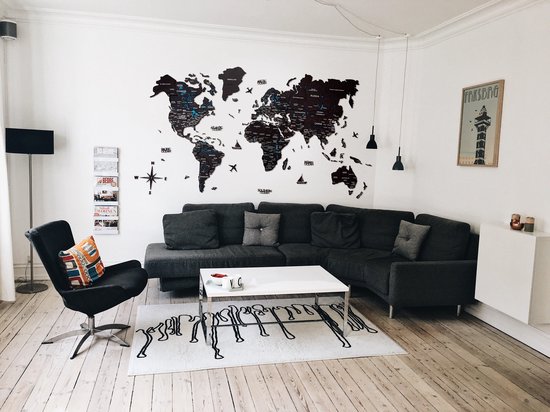 Carte du monde en bois noir sur un mur blanc, au-dessus d'un canapé d'angle gris et d'une table basse blanche.