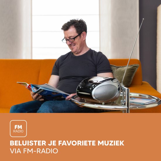 Man met bril leest tijdschrift op oranje bank, luisterend naar muziek via Lenco radio CD-speler.