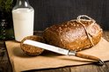 Bruin brood met een gesneden plak, geserveerd met melk en een broodmes met olijfhouten handvat.