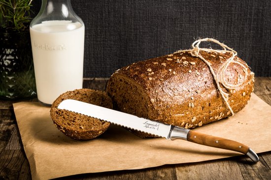 Bruin brood met een gesneden plak, geserveerd met melk en een broodmes met olijfhouten handvat.