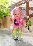 Baby pop met roze 'BE WILD' shirt, groene broek, zilveren laarsjes en een doorzichtige regenjas met regenboogprint.
