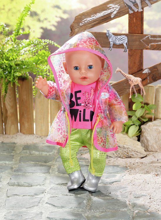 Baby pop met roze 'BE WILD' shirt, groene broek, zilveren laarsjes en een doorzichtige regenjas met regenboogprint.