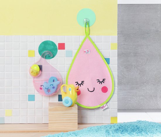 Roze druppelvormige badmat met groene rand. Roze beker met speelgoed aan muur. Gele badeendje op houten blok.