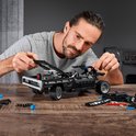Een man bouwt aan een zwarte LEGO Technic Dodge Charger met dikke motor.