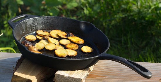 Gietijzeren pan met plakjes aardappel, buiten op houthakblokken.
