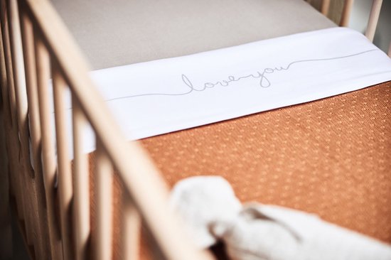 Ledikantlaken met 'love you' tekst in beige op een wit vlak, boven een oranje lakentje met stipjes.
