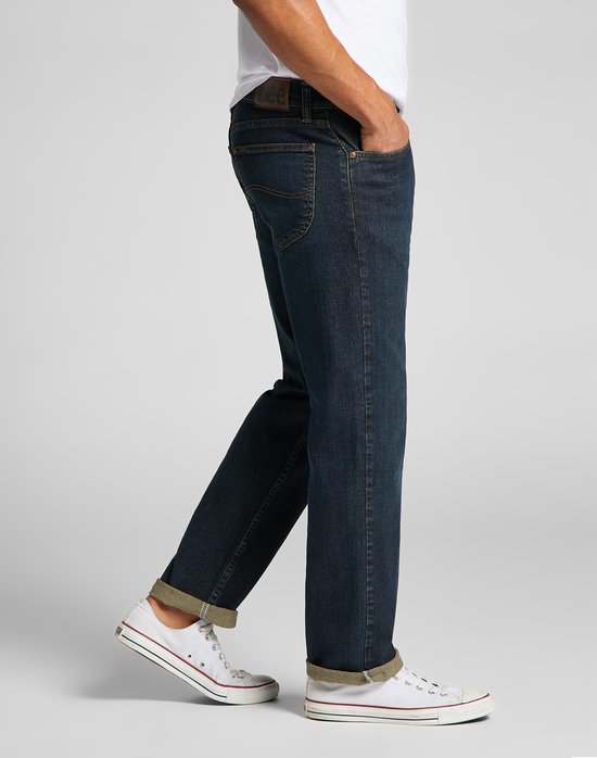 Zijaanzicht van een man in donkerblauwe Lee jeans met omgeslagen pijpen en witte sneakers.