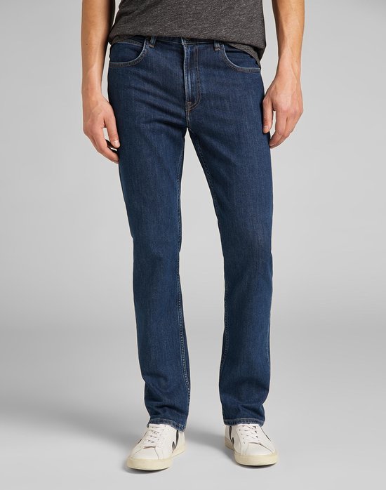 Blauwe jeans met rechte pijpen, gedragen door een man met een grijs T-shirt en witte sneakers.
